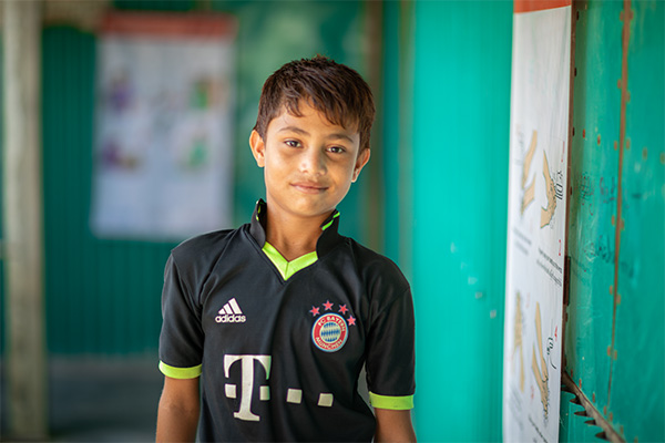 A young Rohingya boy in Bangladesh smiles into the camera.