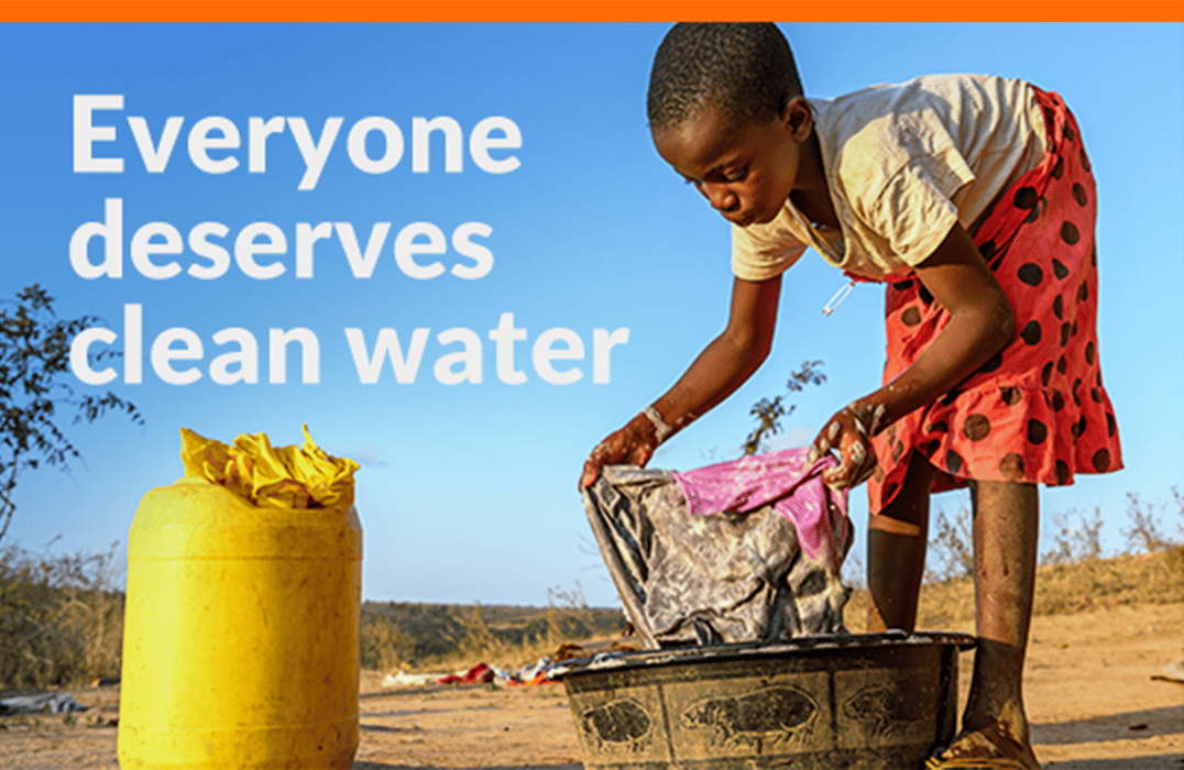 A young girl stands by a bucket washing her clothes.