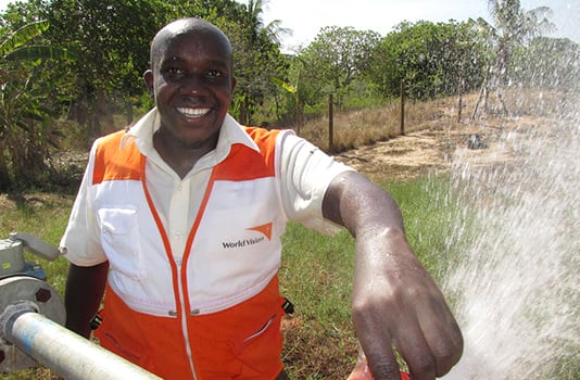 A World Vision staff member smiles while clean water sprays from a water point.