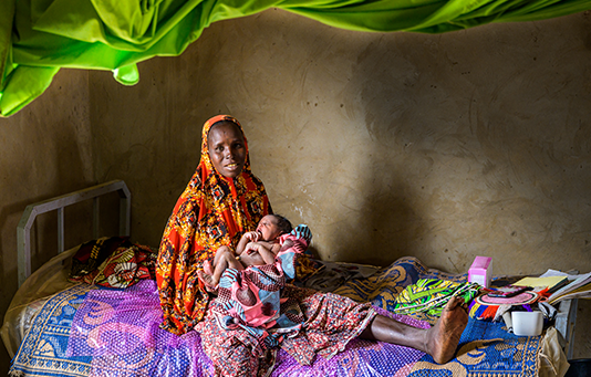 In Niger, a woman holds her newborn son, waiting on a bed to be seen by a doctor.