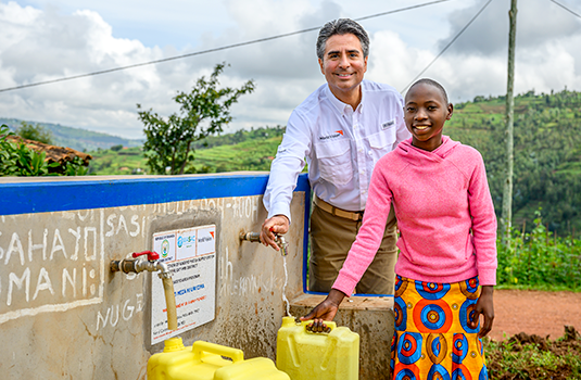 A man and a girl smile while filling a jug with clean water at a water point in Rwanda.