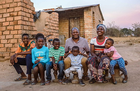 A mother, father, and five children sit outside their home in Zambia.