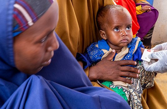 Gloved hands hold a screening band around a baby’s arm, indicating a red box.