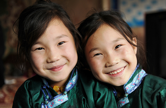 Two girls dressed alike smile at the camera.