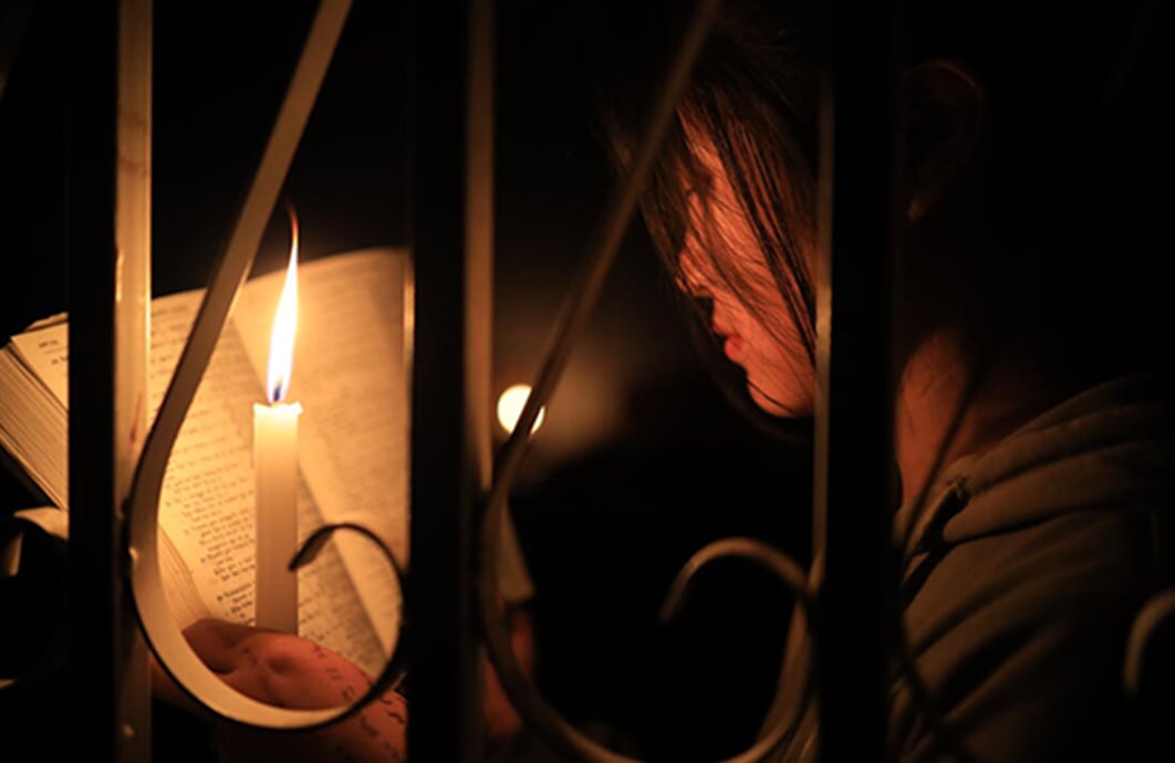 A girl reads by candlelight, her face visible from the side.