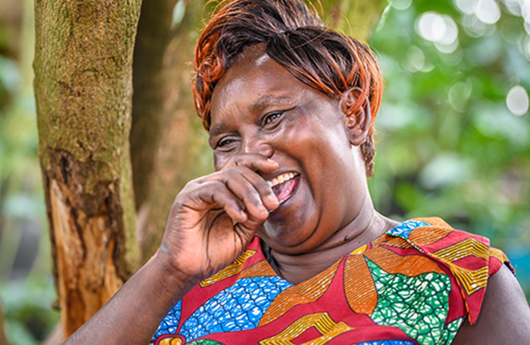 A woman in Kenya wearing colorful clothing laughs with her hand near her mouth.