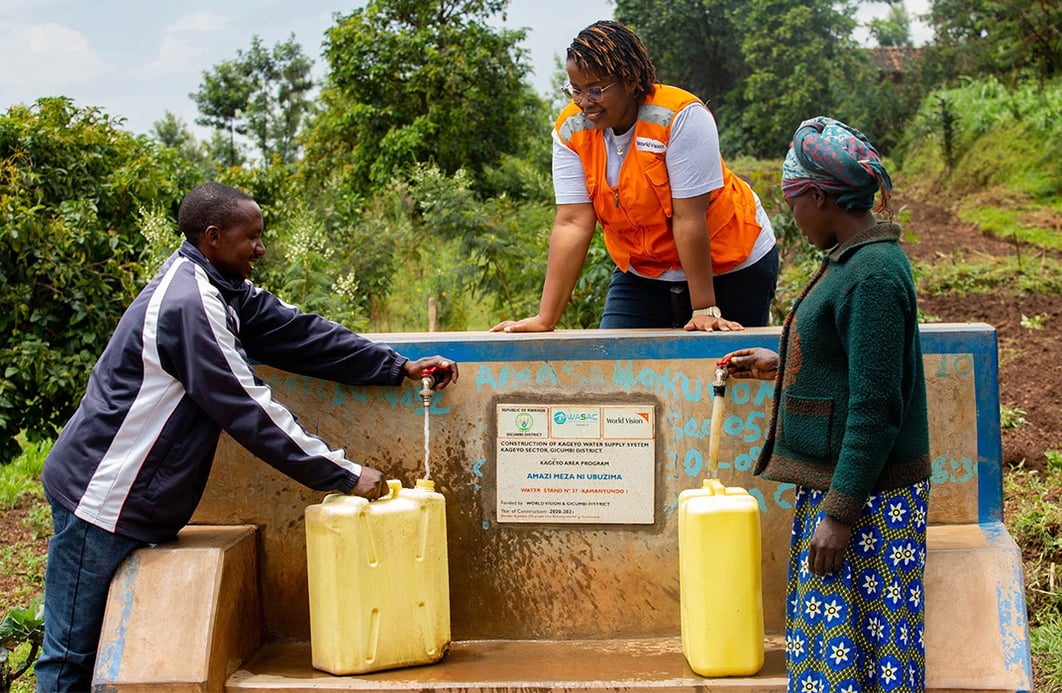 Three people fill water canisters at a water tap station.