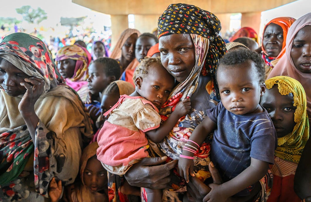 A woman and her two young children stand among a large group of people under a bridge.