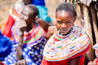 A teenage girl in Samburu, Kenya, wearing a large, beaded collar looks into the camera.