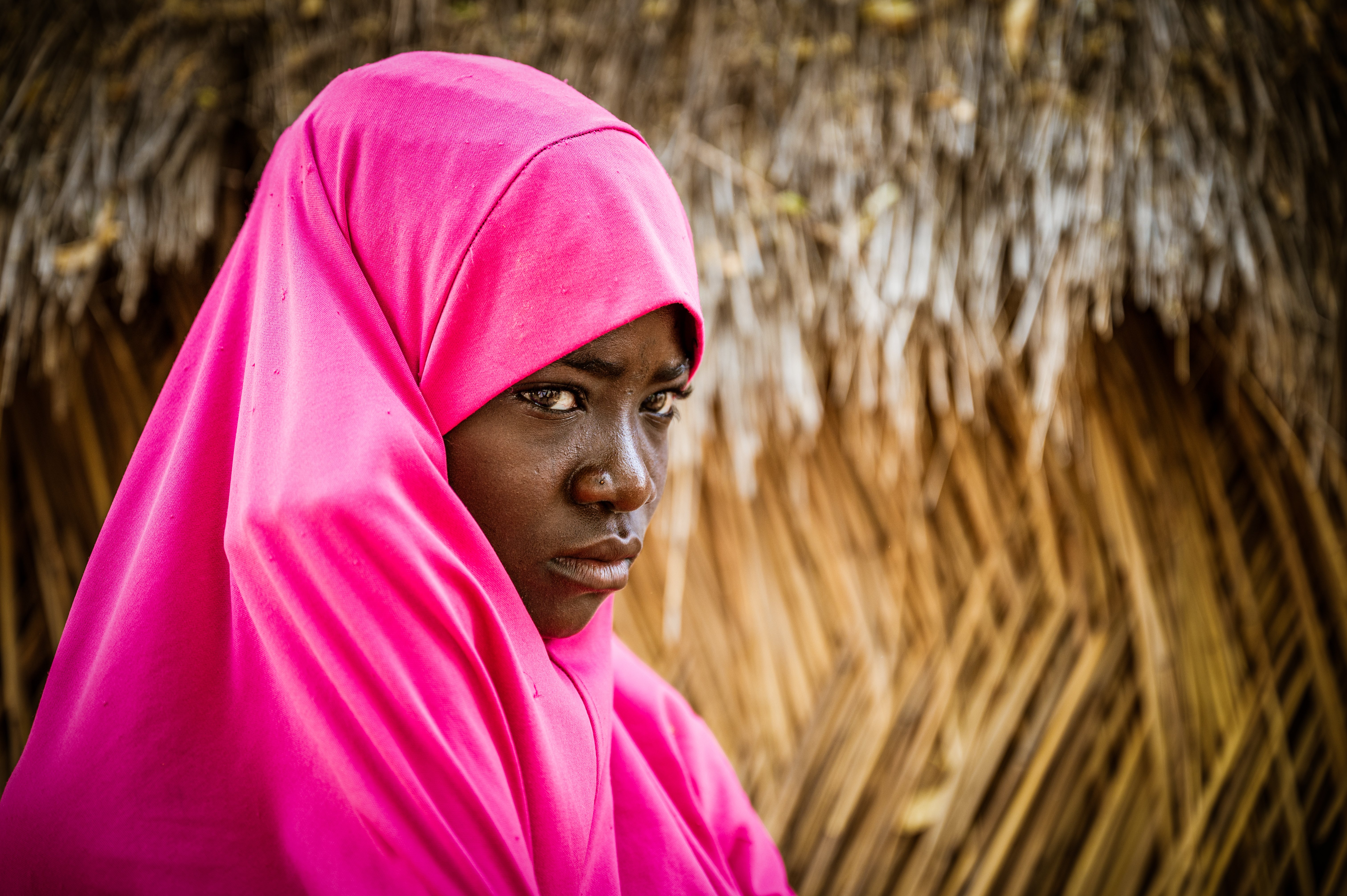 Wearing a rose-colored head covering, a girl has a serious expression on her face.