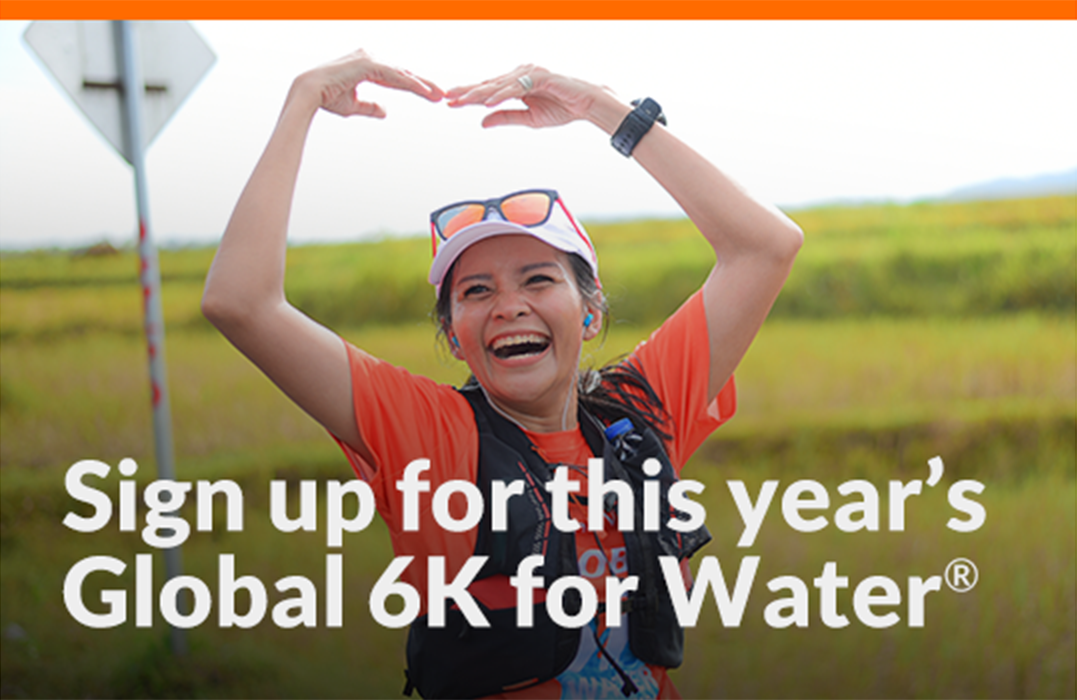 A woman running outside smiles as she makes a heart sign with both arms. Text on image reads: Sign up for this year’s Global 6K for Water®.