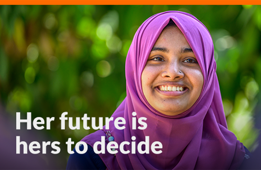 A Bangladeshi woman wearing a purple headdress smiles for the camera