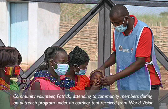 A Zambian community health worker administers medicine to a child held by his mother, who sits near two other women