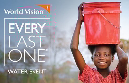 A girl in Zambia carrying a bucket of water on her head smiles at the camera