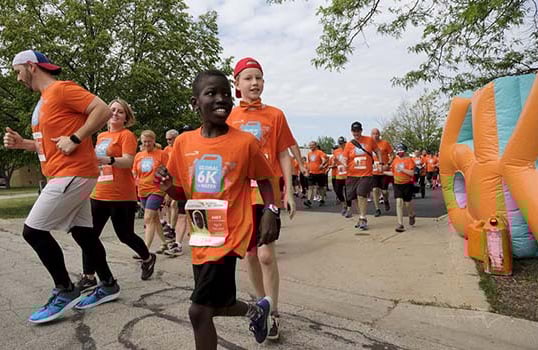 A group of people wearing bright orange t-shirts jog together at the Global 6K run in Palatine, Illinois.