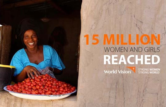 A Rwandan woman wearing a bright blue dress smiles from inside her house; a large plate of tomatoes rests on the open windowsill.
