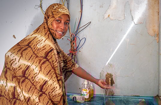 A Nigerien woman wearing a colorful patterned headscarf happily shows the clean water available in all the rooms of a health center.