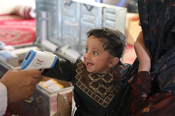 A small child sits in their mother’s lap as their temperature is taken. 