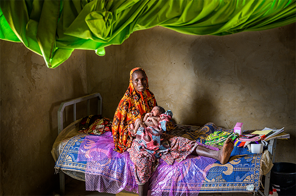 In Niger, a woman holds her newborn son, waiting on a bed to be seen by a doctor.