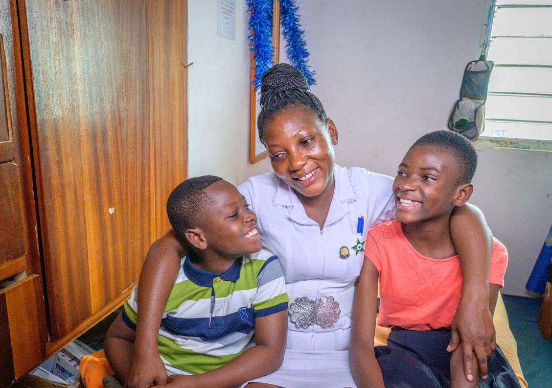A mom hugs her two children, one under each arm.